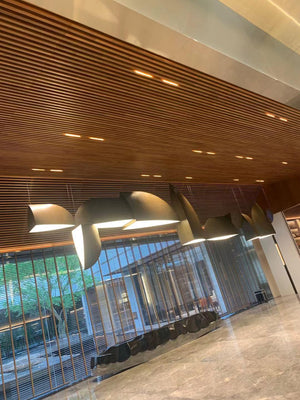 Bronze sail-form pendant chandelier with curved metal panels staggered along a wood-panelled reception ceiling