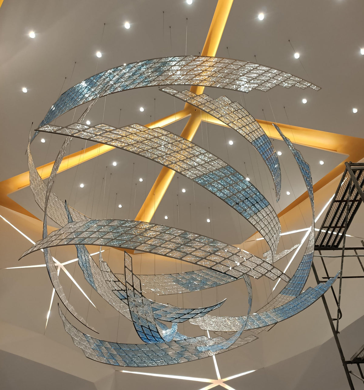 Silver and blue mosaic ribbon chandelier in a swirling vortex form suspended in a grand atrium