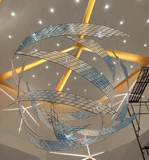 Silver and blue mosaic ribbon chandelier in a swirling vortex form suspended in a grand atrium