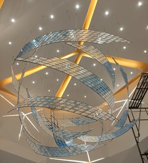 Silver and blue mosaic ribbon chandelier in a swirling vortex form suspended in a grand atrium