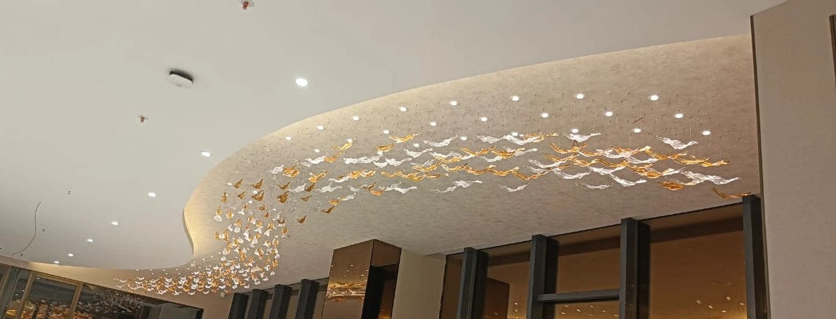 Hand-blown amber and clear glass leaf chandelier following a curved ceiling at a Signature Global site in Noida