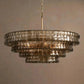 Warm-lit view of the concentric tiered chandelier showing hammered bronze glass ribbons and a brass suspension rod