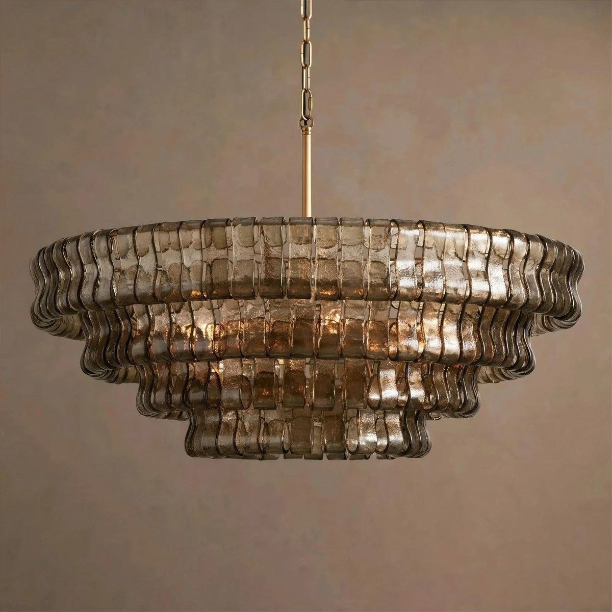 Warm-lit view of the concentric tiered chandelier showing hammered bronze glass ribbons and a brass suspension rod